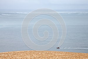 Boat sailing on the Atlantic ocean during a rain story under a cloudy sky passing next to the Pyla Dune.