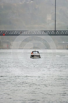 Boat sailing below the lower platform of the Don Luis steel bridge, with people walking with umbrellas due to the light rain and