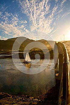 Boat sailing under bridge in evening light in Lofoten fjord in Norway