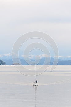 Boat sailing on a windless lake with cloudy sky