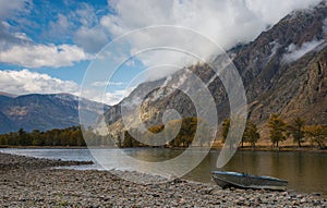 Boat On The Shore. Autumn Mountain Landscape With A River Valley, Beautiful Cloudy Sky And Aluminum Boat On A Stony Shore.