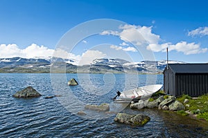 Boat on the shore of Lake Finsevatnet, snowy mountains and glacier Hardangerjokulen in Finse, Norway