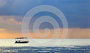 Boat silhouette at sunset in an ocean in pastel colors.