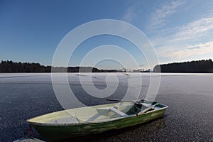 A boat stuck in the ice of a forest lake during winter, illuminated by the harsh daylight amidst freezing temperatures.