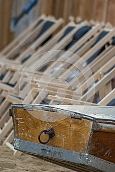 The boat tail of a wooden rowing boat and in the background a series of suspended empty deckchairs lined up in order on the beach