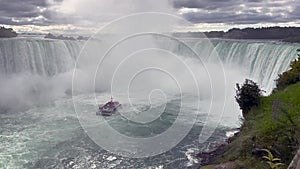 A boat with tourists is driving close to the famous `The Horseshoe Falls` and partly disappears in the spume