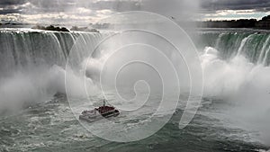 A boat with tourists is driving close to the famous `The Horseshoe Falls` and partly disappears in the spume