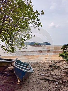Boat and tree foreground and small tropical island in the middle of sea and cloudy blue sky background at low tide period
