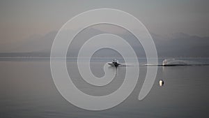 Boat with water skier driving by a pier during sunrise