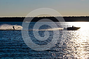 A boat and water skier silhouetted against a blue lake