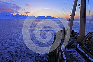 Boat in winter Arctic. White snowy mountain, blue glacier Svalbard, Norway. Ice in ocean. Iceberg twilight in North pole. Pink clo