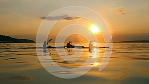 Boaters are kayaking at sunset in a side view
