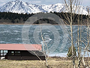 Boathouse by icy lake with snowy mountain