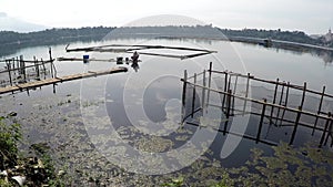 Boatman paddles bamboo raft across polluted lake fish pens