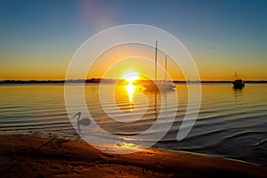 Boats anchored in Bribie Island Australia bay at sunset as sun disappears over the horizon with light spilling across dark water