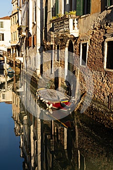 Boats covered from rain parked in the water next to the house in canal of Venice.
