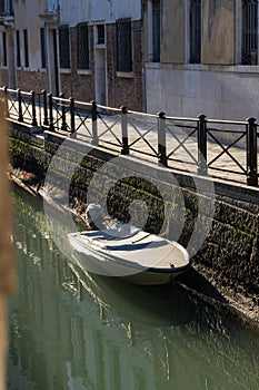Boats covered from rain parked in the water next to the house in canal of Venice.