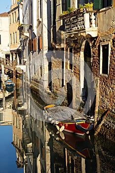 Boats covered from rain parked in the water next to the house in canal of Venice.