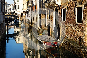 Boats covered from rain parked in the water next to the house in canal of Venice.