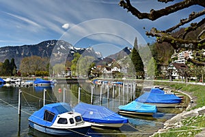 Boats covered with tarpaulin moored on Walensee lake. View of the Alps. Weesen, Switzerland