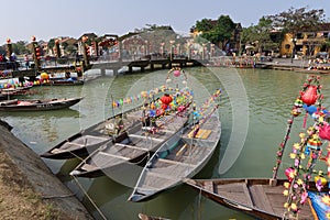 Boats decorated with lanterns anchored in the Thu Bon river next to the famous Hoi An Bridge