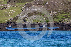 Boats docked in the bay among rocks on Inishbofin Island with a rocky mountain in the background photo