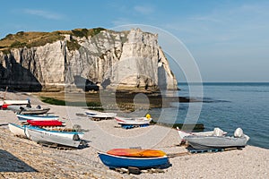 Boats in front of the halk cliffs of Etretat with the natural arch Porte d`Aval and the stone needle called L`Aiguille