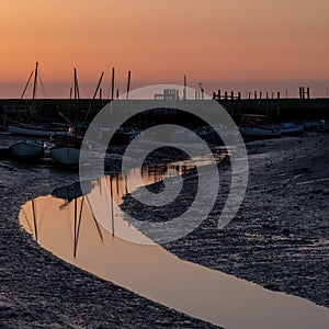 Boats at low tide, moored at the quay at Morston near Holt on the North Norfolk coast, East Anglia UK. Photographed at sundown.