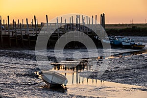 Boats at low tide, moored at the quay at Morston near Holt on the North Norfolk coast, East Anglia UK. Photographed at sundown.