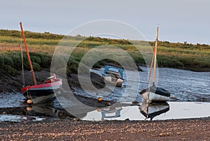 Boats at low tide, moored at the quay at Morston near Holt on the North Norfolk coast, East Anglia UK. Photographed at sundown.