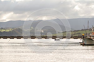 Boats moored in port with the bridge of San Vicente de la barquera, Cantabria, mountains and cloudy sky in the background