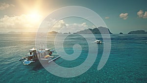 Boats at ocean coast with sun over mountain island aerial view. Cruise at sea bay with green tropic