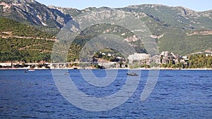 Boats and a skiff float on the sea against the backdrop of a city in the middle of huge mountains covered with green