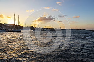 Boats in Vlichada harbor on Santorini island in Greece in the morning at sunrise. The background is a blue sky with white clouds