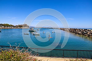 Boats and yachts docked in the deep blue ocean water of the Dana Point Harbor with people and colorful paddle boards