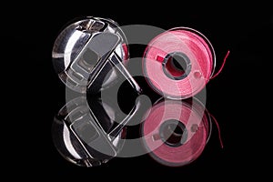 Bobbin case and plastic bobbin mirrored on black background