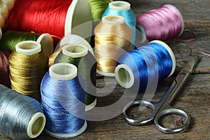 Bobbin with colorful threads and scissors on a wooden background, close-up, selective fokus