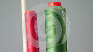 A bobbin of red and green cotton thread on the spindle of the sewing machine in the foreground, close-up. sewing factory