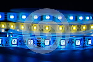 Bobbin with roll of glowing LED strip lighting placed on table, blue and warm white color in dark room