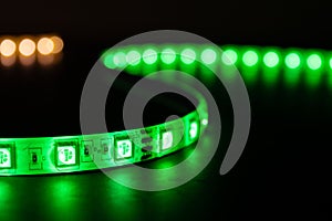 Bobbin with roll of glowing LED strip lighting placed on table, green and warm white color