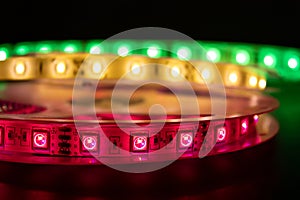 Bobbin with roll of glowing LED strip lighting placed on table, pink, green and warm white color