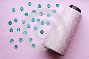 Bobbin with thread and blue buttons on a pink background close-up, concept of accessories for sewing