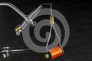 Bobbin of thread hanging from a hook on a fly tying vise