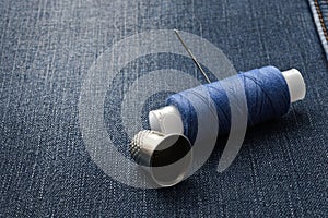 A bobbin of thread with a needle and a thimble. on denim background. close-up