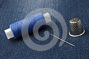 A bobbin of thread with a needle and a thimble. on denim background. close-up