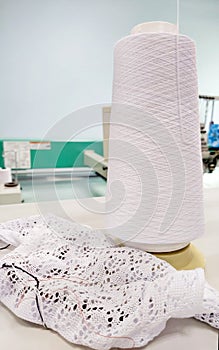 A bobbin of white cotton yarn in production and a product made from this thread