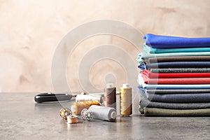 Bobbins with threads and stack of colorful fabrics on table. Tailoring accessories
