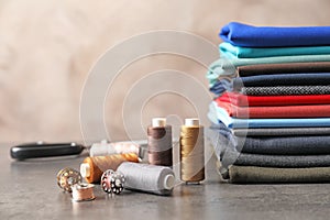 Bobbins with threads and stack of fabrics on table. Tailoring accessories