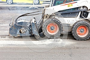 A bobcat with a surface repair attachment on asphalt plows the old surface on an asphalt road