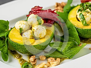 Bocconcini cheese balls in halves of avocado served with salad on white plate